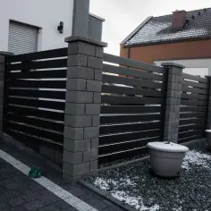 Nowoczesne ogrodzenie z ciemnymi panelami i kamiennymi słupkami. Maksymalna wysokość ogrodzenia zapewnia prywatność. Dwa duże donice z zimowym szronem.
