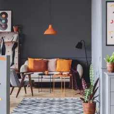 Nowoczesny salon z sofą, fotelami i stolikami. Dominują zimne kolory ścian i mebli, przełamane ciepłymi akcentami poduszek i dekoracji.