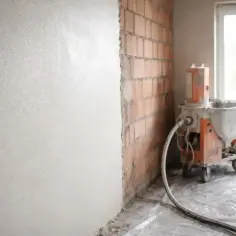 Maszyna do tynkowania nakłada tynki cementowo wapienne na ścianę z cegły.