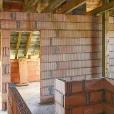 Budowa domu w toku. Widać ściany z pustaków ceramicznych, drewniane belki stropowe i konstrukcję ścianki kolankowej.