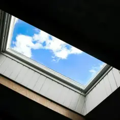 Widok na błękitne niebo z chmurami przez nowoczesne okna dachowe. Okna dachowe wymiary dopasowane do poddasza.