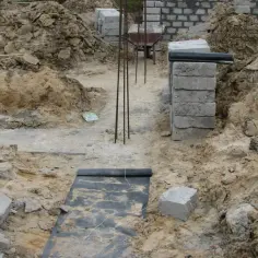 Budowa trwa, widać wykopy pod stopy fundamentowe, zbrojenie i materiały budowlane.
