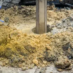 Wiertnica zagłębia się w ziemię, tworząc otwór pod pale fundamentowe. Wokół błoto i gruz.