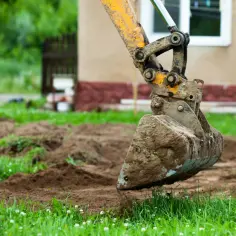Koparka pracuje nad wyrównaniem działki ze spadkiem, przesuwając ziemię.