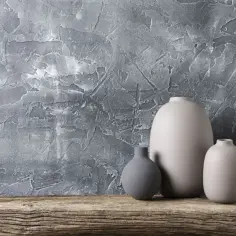 Trzy ceramiczne wazony na drewnianej półce, na tle ściany z szarymi tynkami strukturalnymi o wyrazistych wzorach.