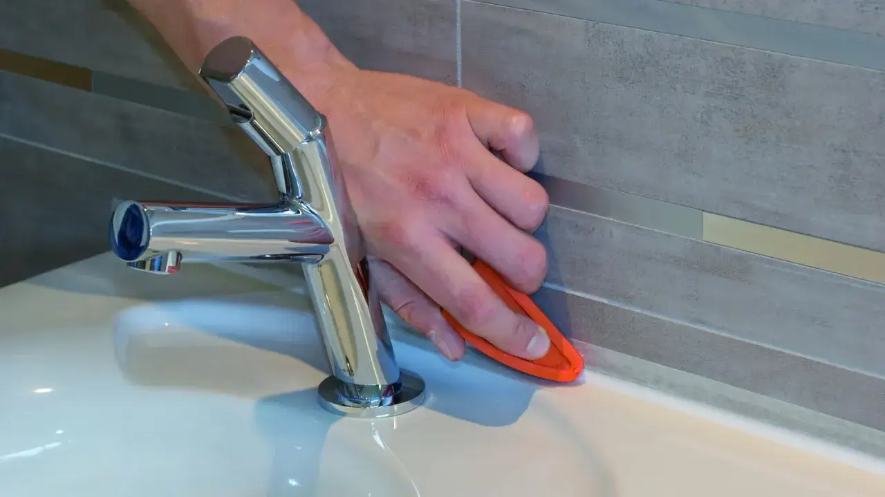 Dłoń wygładza silikon sanitarny przy wannie. Czas schnięcia silikonu sanitarnego zależy od warunków.