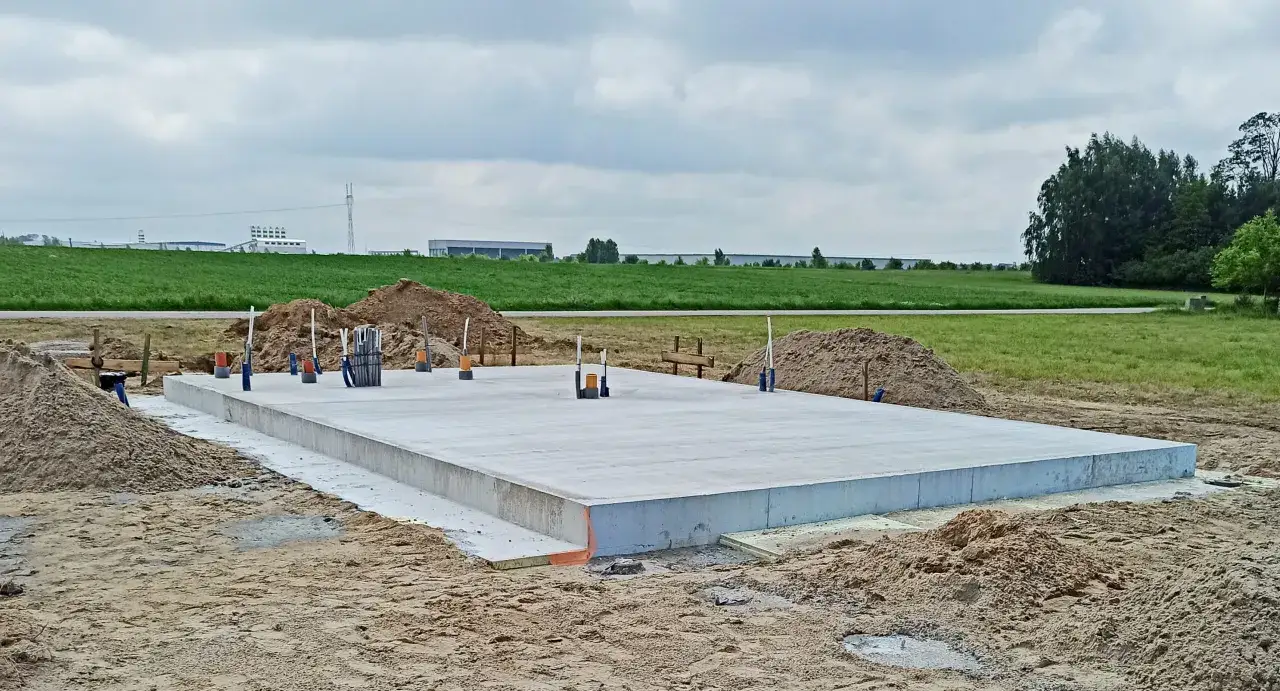 Solidny beton na fundament gotowy do budowy. Wokół plac budowy z piaskiem i zielone pola w tle.