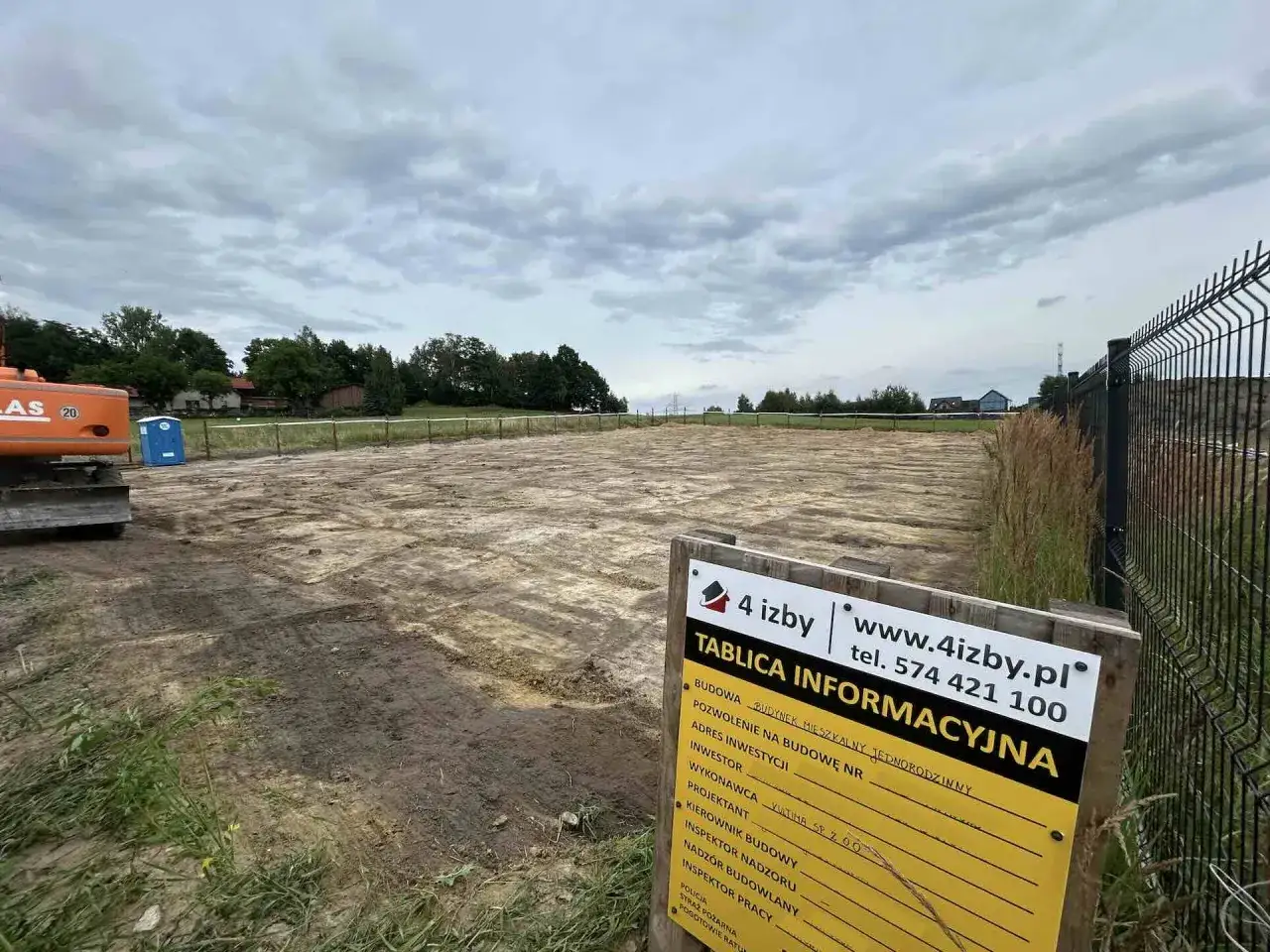 Teren budowy z koparką i tablicą informacyjną. Rozpoczyna się budowa budynku mieszkalnego.